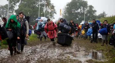 Penonton Festival Glastonbury tampak melewati jalanan yang banjir dan berlumpur saat tiba di Worthy Farm, Somerset, Inggris, (22/6). Festival Glastonbury merupakan festival musik paling populer di dunia. (REUTERS / Stoyan  Nenov)