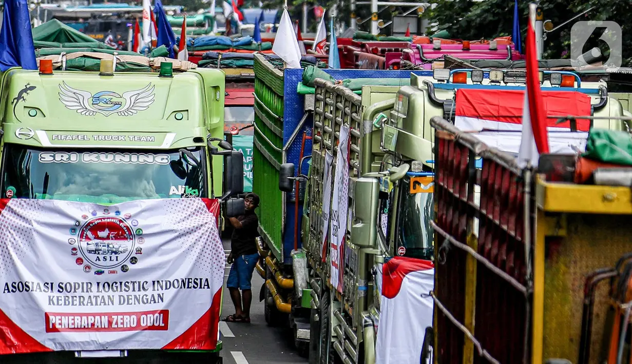 Salah satu peserta aksi terlihat di antara truk-truk saat unjuk rasa terkait Rancangan Undang Undang (RUU) nol kelebihan muatan dan dimensi atau Zero Over Dimension Over Load (ODOL) memasang spanduk di Jalan Medan Merdeka Selatan, Jakarta, Rabu (2/7/2025). (Liputan6.com/Herman Zakharia)