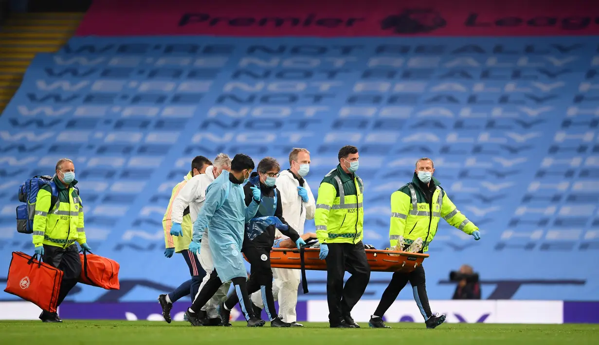 Petugas medis dalam APD lengkap membawa pemain Manchester City Eric Garcia yang cedera saat menghadapi Arsenal pada laga Premier League di Etihad Stadium, Manchester, Inggris, Rabu (17/6/2020). Manchester City menang dengan skor 3-0. (LAURENCE GRIFFITHS/POOL/AFP)