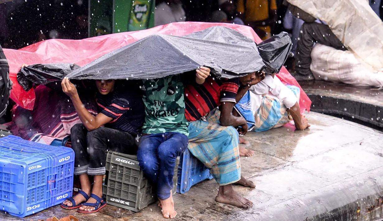 Warga Bangladesh melindungi diri mereka dari hujan saat duduk di atas atap kereta untuk menuju kampung halaman di Dhaka pada 4 Juni 2019. Sebagaimana terjadi di Indonesia, masyarakat Bangladesh pun memiliki tradisi mudik saat Idul Fitri, namun agak membahayakan keselamatan. (MUNIR UZ ZAMAN/AFP)