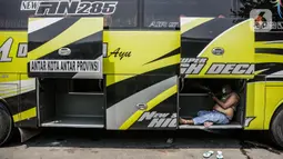 Seorang awak bus antarkota antarprovinsi (AKAP) beristirahat di armadanya di Terminal Kalideres, Jakarta, Senin (26/4/2021). Pemerintah memperpanjang masa larangan mudik Lebaran yaitu mulai dari 22 April hingga 24 Mei 2021. (Liputan6.com/Faizal Fanani)