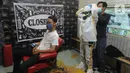 Seorang tukang cukur memakai alat pelindung diri (APD) buatannya sendiri sebelum mencukur pelanggannya di Chemot Barbershop, Ciawi, Bogor, Jawa Barat, Minggu (5/4/2020). (merdeka.com/Arie Basuki)