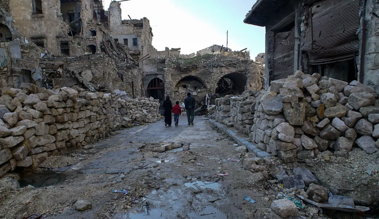 Sebuah keluarga berjalan diantara reruntuhan bangunan pasar lama di kota tua Aleppo, Suriah (21/1). Pada tahun 1986, kota kuno Aleppo dinyatakan sebagai situs warisan dunia UNESCO. (AP Photo / Mstyslav Chernov)