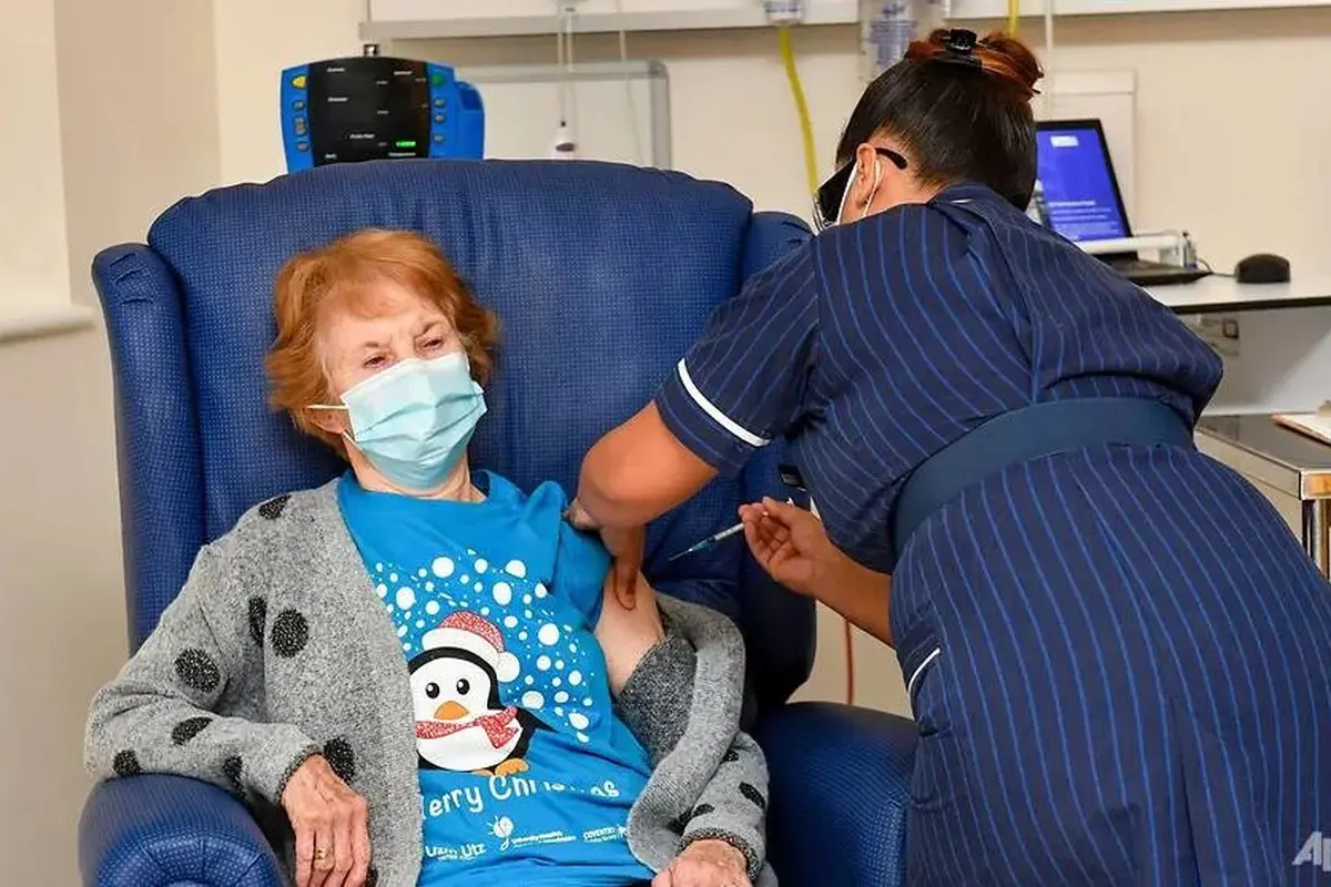Margaret Keenan, 90 tahun, pasien pertama di Inggris yang menerima vaksin Pfizer-BioNTech COVID-19, diberikan oleh perawat May Parsons di University Hospital, Coventry, Inggris, 8 Des 2020. (Jacob King / Pool via AP)