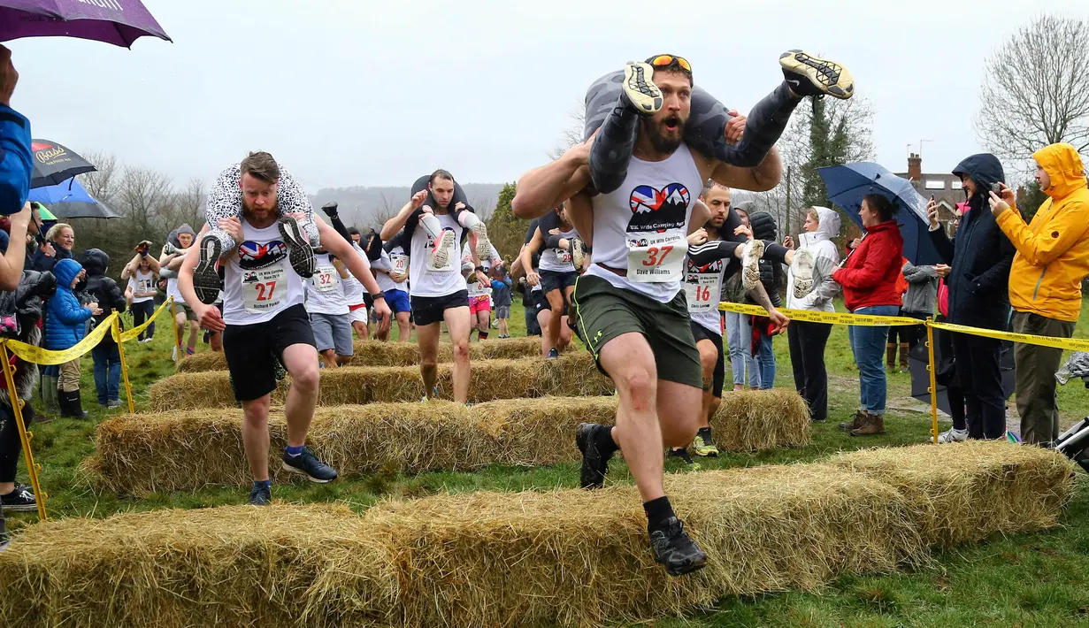 Para peserta melewati rintangan saat Lomba Lari Gendong Istri di The Nower, Dorking, Inggris, Minggu (3/3). Tidak sedikit di antara para suami yang kesulitan saat berlari sambil menggendong istri mereka. (Gareth Fuller/PA via AP)