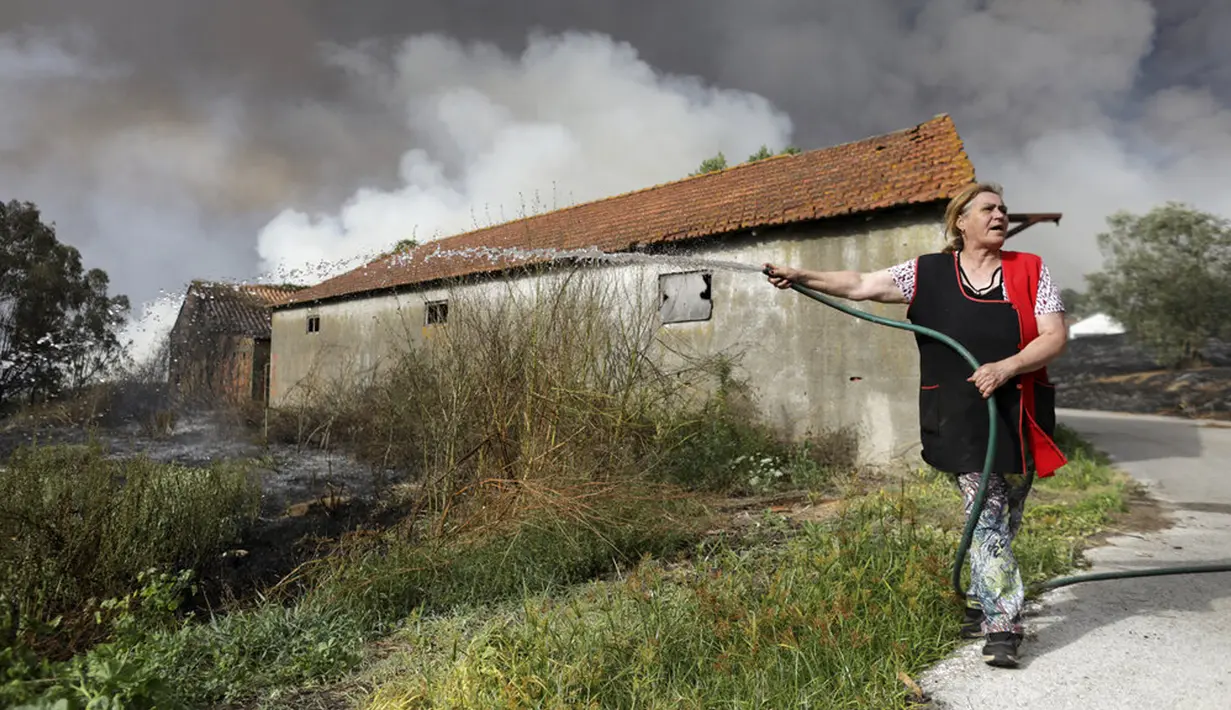 Seorang penduduk setempat menggunakan selang taman untuk mencoba mencegah kebakaran hutan mencapai rumah-rumah di Desa Figueiras, di luar Leiria, Portugal, 12 Juli 2022. Ratusan petugas pemadam kebakaran di Portugal terus memadamkan api di pusat negara yang memaksa evakuasi puluhan orang dari rumah mereka sebagian besar di desa-desa sekitar Santarem, Leiria, dan Pombal. (AP Photo/Joao Henriques)
