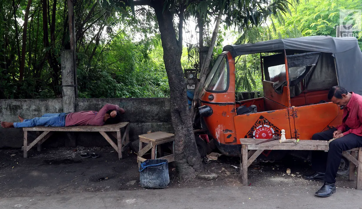 Dua orang pria melakukan aktivitas di dekat bangkai bajaj oranye di kawasan Roxy, Jakarta Barat, Selasa (27/2). Seiring berkembangnya kebutuhan transportasi yang murah dan cepat, kini bajaj oranye sudah tak lagi digunakan. (Liputan6.com/JohanTallo)