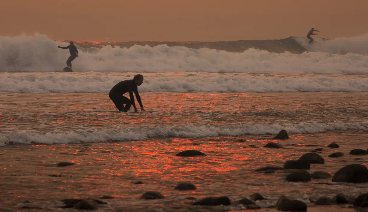 Sejumlah orang berselancar di pantai Carpinteria, California (12/12). Warnya oranye keemasan tersebut karena cahaya matahari yang terhalang oleh asap kebakaran dari Api Thomas. (David McNew / Getty Images / AFP)