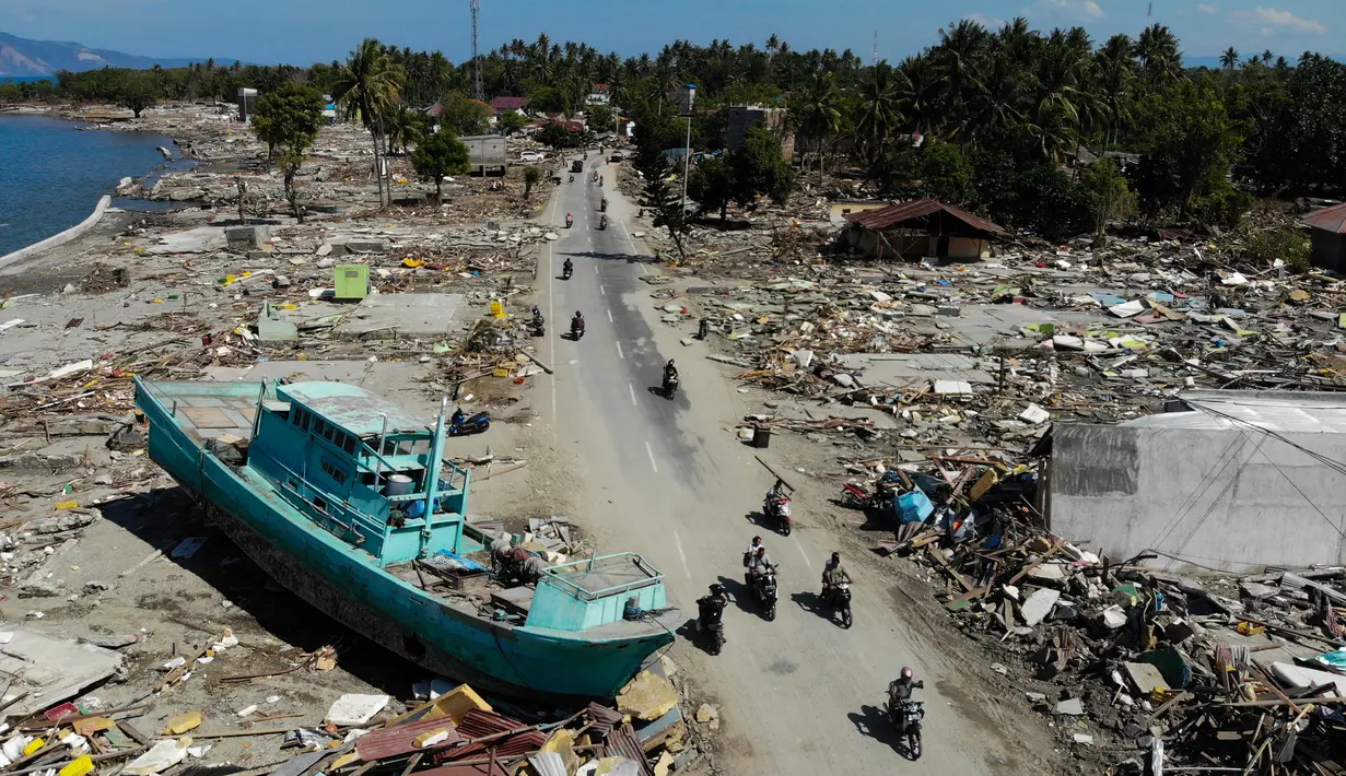 Pengendara sepeda motor melewati perahu dan rerntuhan bangunan usai gempa dan tsunami melanda Palu, Sulawesi Tengah, Senin (1/10). Pihak berwenang tengah menyiapkan kuburan massal untuk memakamkan ratusan korban tewas. (JEWEL SAMAD/AFP)