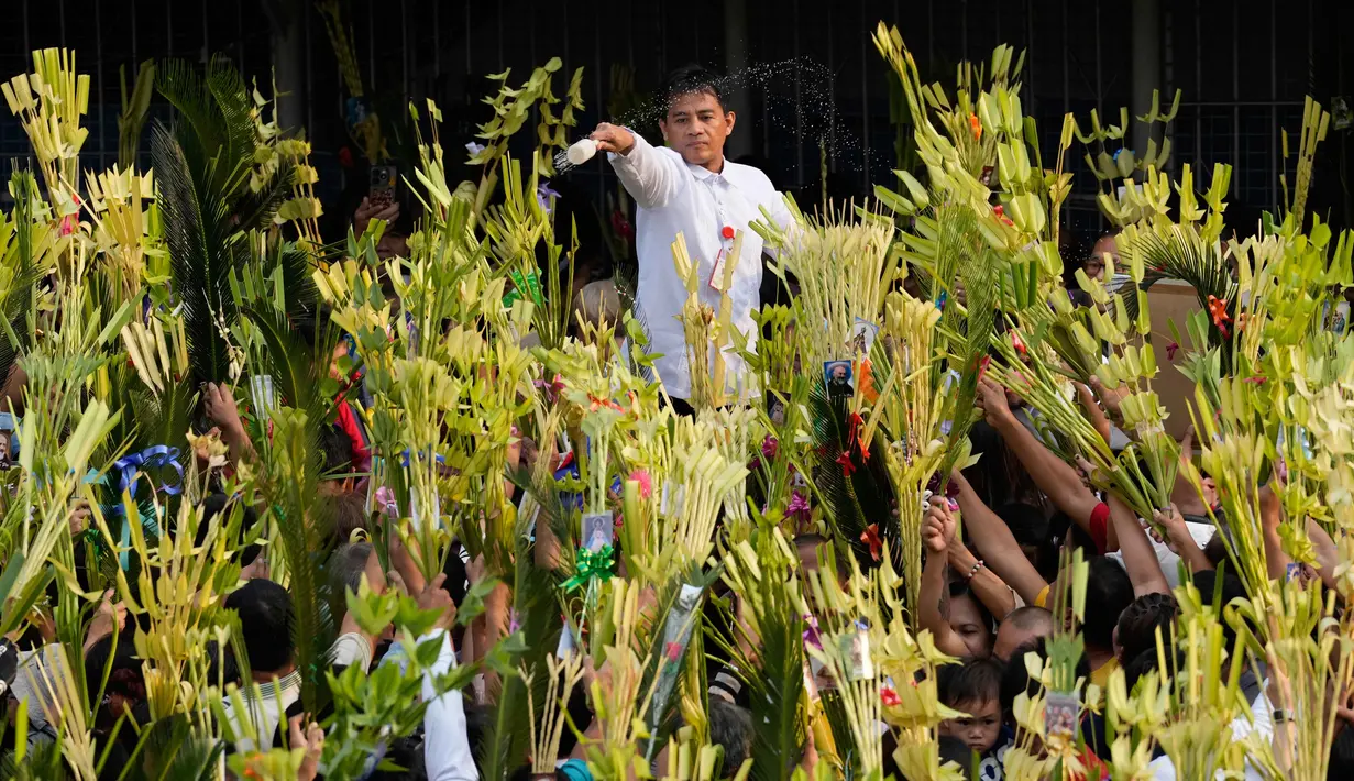 Pada hari ini, Minggu 29 Maret 2026, umat Kristiani beramai-ramai membawa daun palem untuk diberkati ke gereja sebagai simbol penghormatan dan kemenangan, menyambut Yesus sebagai Raja dalam kehidupan sehari-hari. Tampak dalam foto, seorang pekerja gereja memercikkan air suci ke daun palem para umat selama upacara pemberkatan di luar Katedral Antipolo, kota Antipolo, provinsi Rizal, Filipina, saat memperingati Minggu Palma, 29 Maret 2026. (AP Photo/Aaron Favila)