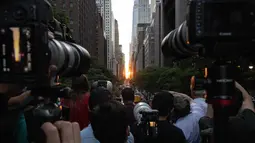 Orang-orang mengambil gambar saat matahari terbenam di Manhattan ketika fenomena "Manhattanhenge" di 42nd street, New York, Senin (11/7/2022). Fenomena Manhattanhenge hanyaterjadi di musim panas, tepatnya diantara bulan Mei hingga Juli. (Yuki IWAMURA / AFP)