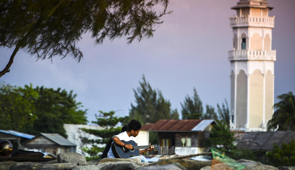 Seorang pria memainkan gitar sambil menikmati matahari terbenam di pantai di Banda Aceh (7/4). Sebagai pusat pemerintahan, Banda Aceh menjadi pusat kegiatan ekonomi, politik, sosial dan budaya. (AFP Photo/Chaideer Mahyuddin)