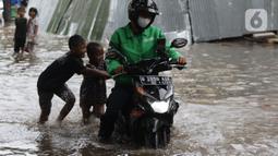 Anak-anak mendorong motor pengemudi ojol melewati sebagian Jalan Bungur Besar Raya yang tergenang air, Jakarta, Selasa (18/1/2022). Genangan air membuat arus lalu lintas di sekitar depan PN Jakarta Pusat menjadi terganggu dan tersendat. (Liputan6.com/Helmi Fithriansyah)