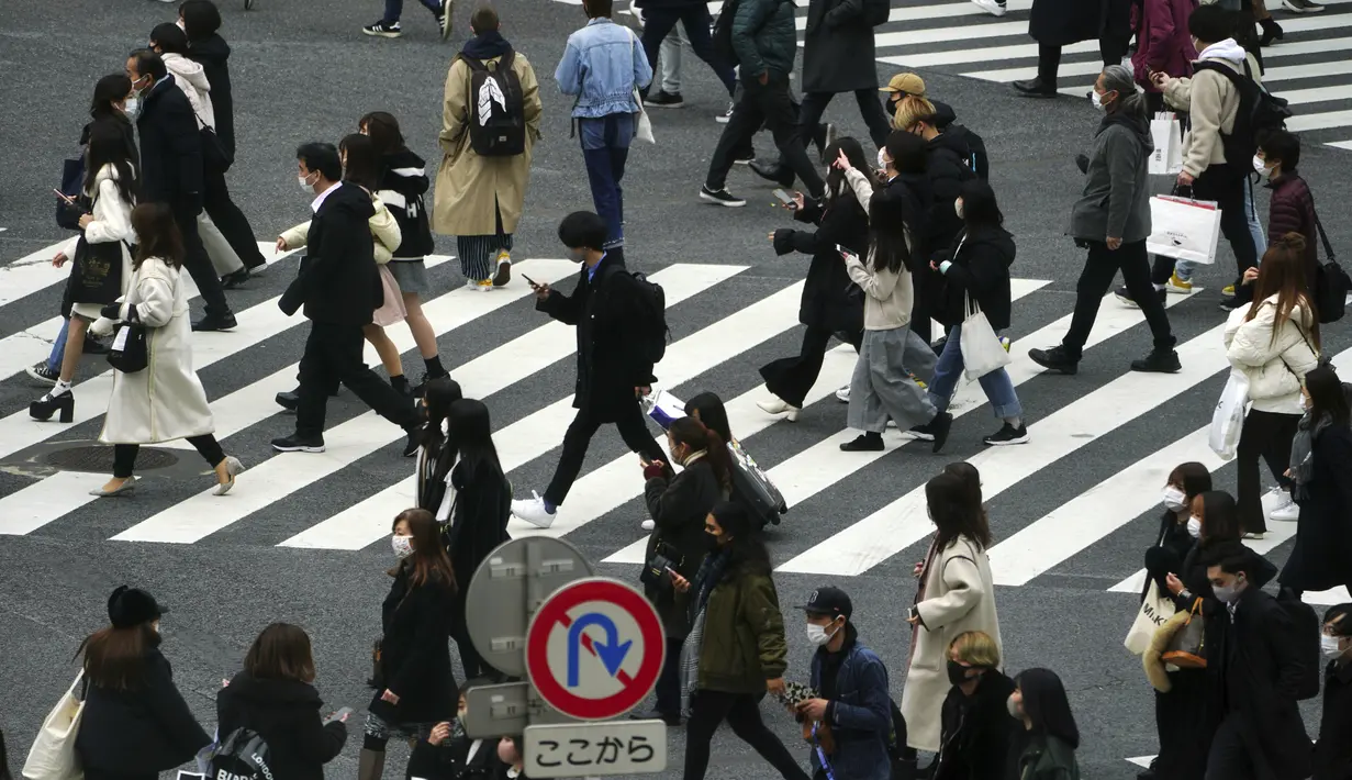 Orang-orang yang mengenakan masker berjalan di sepanjang penyeberangan pejalan kaki di daerah Shibuya, Tokyo, Selasa (5/1/2021). Pemerintah Jepang sedang mempertimbangkan mendeklarasikan keadaan darurat untuk Tokyo karena kasus infeksi virus corona yang terus meningkat. (AP Photo/Eugene Hoshiko)