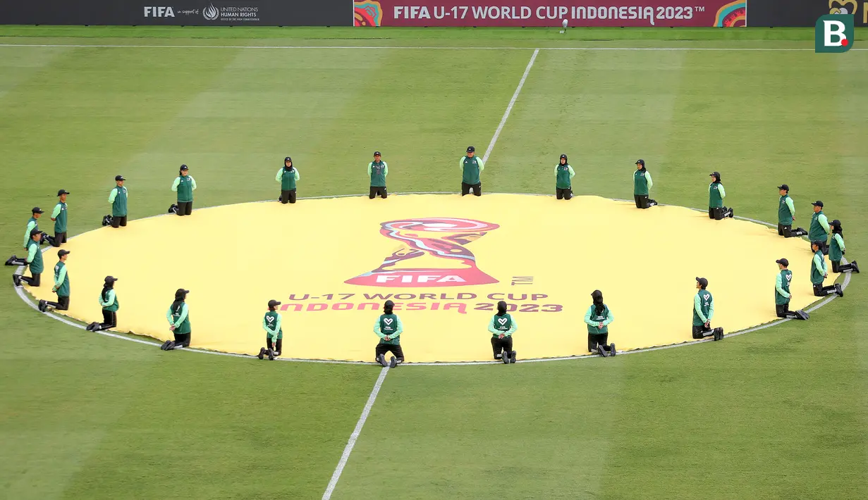 Sejumlah petugas membentangkan benedera di tengah lapangan sebelum laga Piala Dunia U-17 2023 antara Timnas Mali U-17 melawan Timnas Kanada U-17 di Stadion Gelora Bung Tomo (GBT), Surabaya, Kamis (16/11/2023). (Bola.com/Bagaskara Lazuardi)