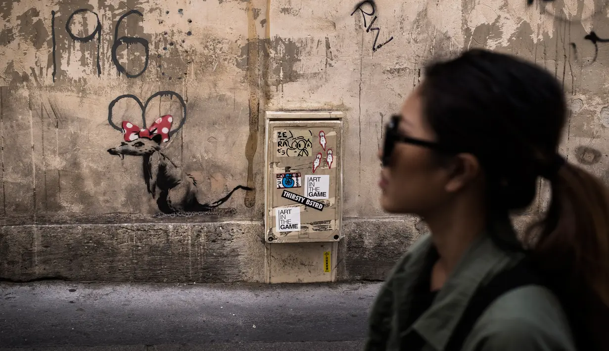 Seorang wanita berjalan melewati mural yang diduga karya seniman sekaligus aktivis Banksy di Paris, Prancis, Minggu (24/6). Karya seni ini muncul bertepatan dengan Hari Pengungsi Dunia. (PHILIPPE LOPEZ/AFP)