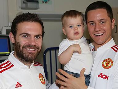 Pemain Manchester United, Ander Herrera, menggendong seorang anak yang sedang sakit saat mengunjungi Rumah Sakit Royal Manchester Children bersama rekan setimnya, Juan Mata. (www.manutd.com)