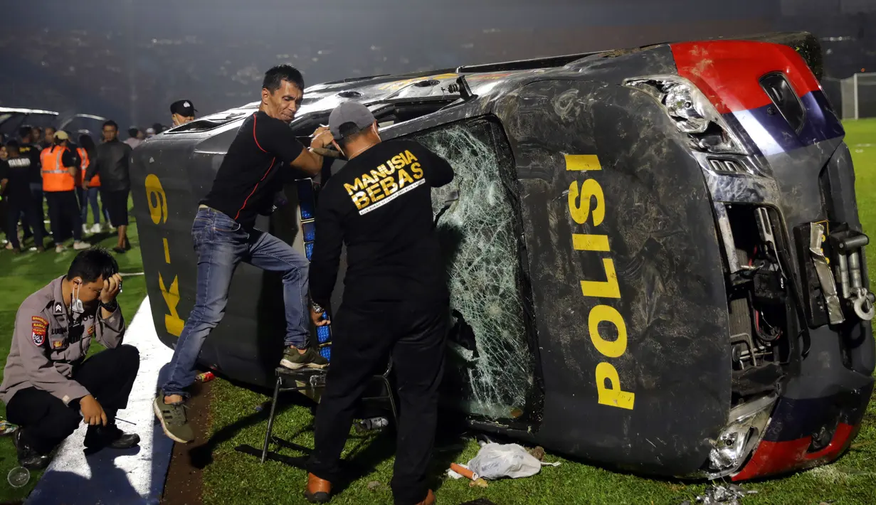 Petugas memeriksa kendaraan polisi yang rusak menyusul kerusuhan pada pertandingan sepak bola antara Arema Vs Persebaya di Stadion Kanjuruhan, Malang, Jawa Timur, 1 Oktober 2022. Selain korban meninggal dunia, tercatat ada 13 unit kendaraan yang mengalami kerusakan, 10 di antaranya merupakan kendaraan Polri. (AP Photo/Yudha Prabowo)