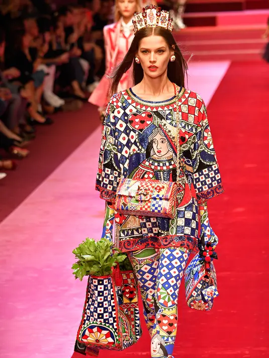 Seorang model berjalan di atas catwalk dengan membawa tas besar mirip tas pasar dan mengisinya dengan sayuran untuk koleksi Dolce & Gabbana Spring/Summer 2018 di Milan Fashion Week, Minggu (24/9). (AFP PHOTO / Andreas SOLARO)