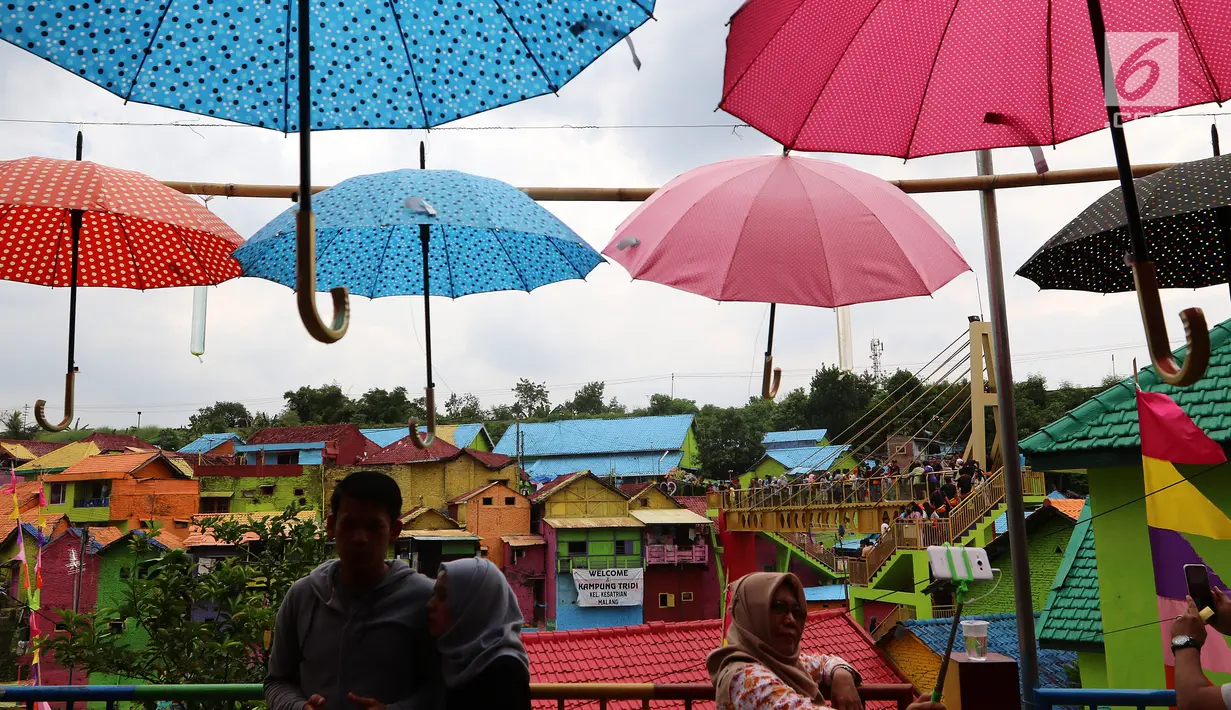 Wisatawan sedang berbincang dan selfie di kampung warna-warni, Kelurahan Kesatrian, Kota Malang, Minggu (5/11). Lukisan di kampung tersebut melibatkan komunitas mural dan seniman. (Liputan6.com/Fery Pradolo)