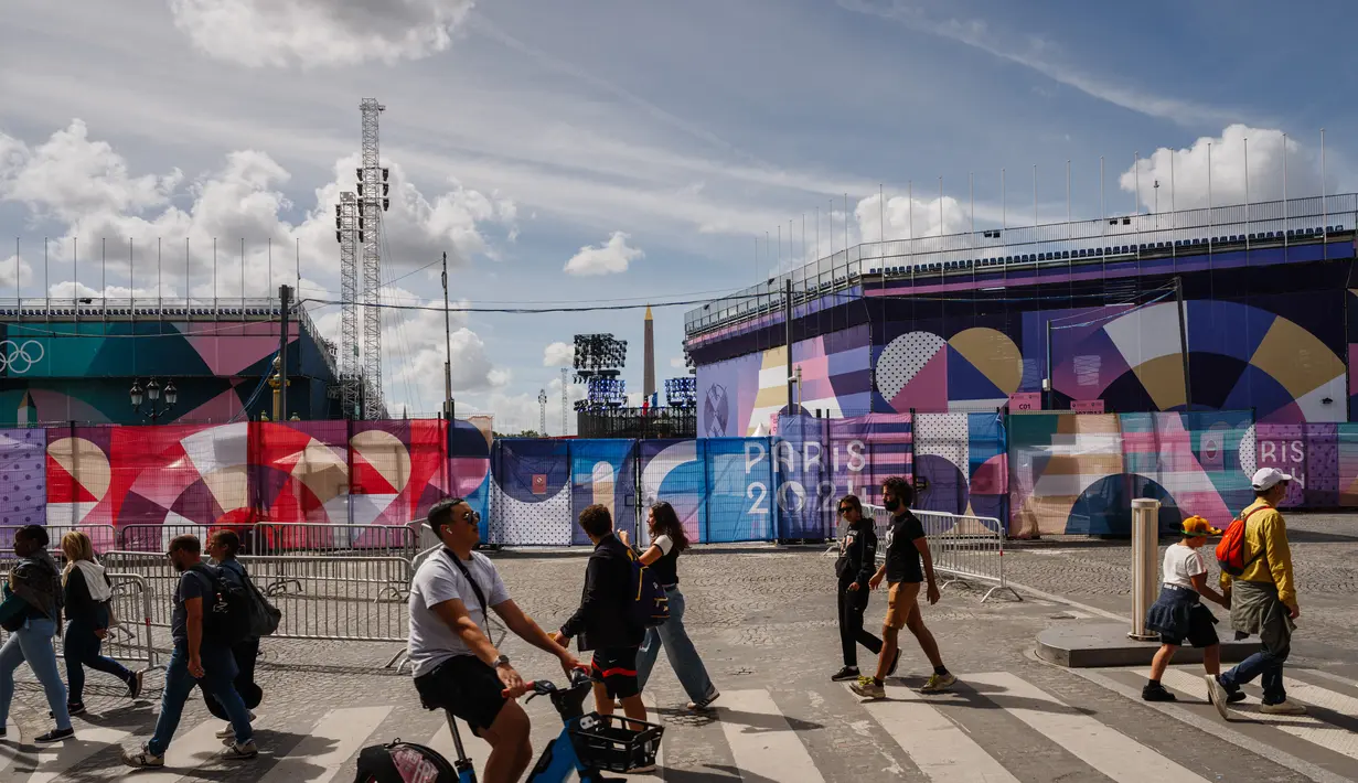 Pejalan kaki berjalan di dekat situs Paralimpiade Place de la Concorde yang ditutupi terpal "Paris 2024" menjelang ajang Paralimpiade 2024 di paris, Rabu (21/8/2024). (Dimitar DILKOFF / AFP)