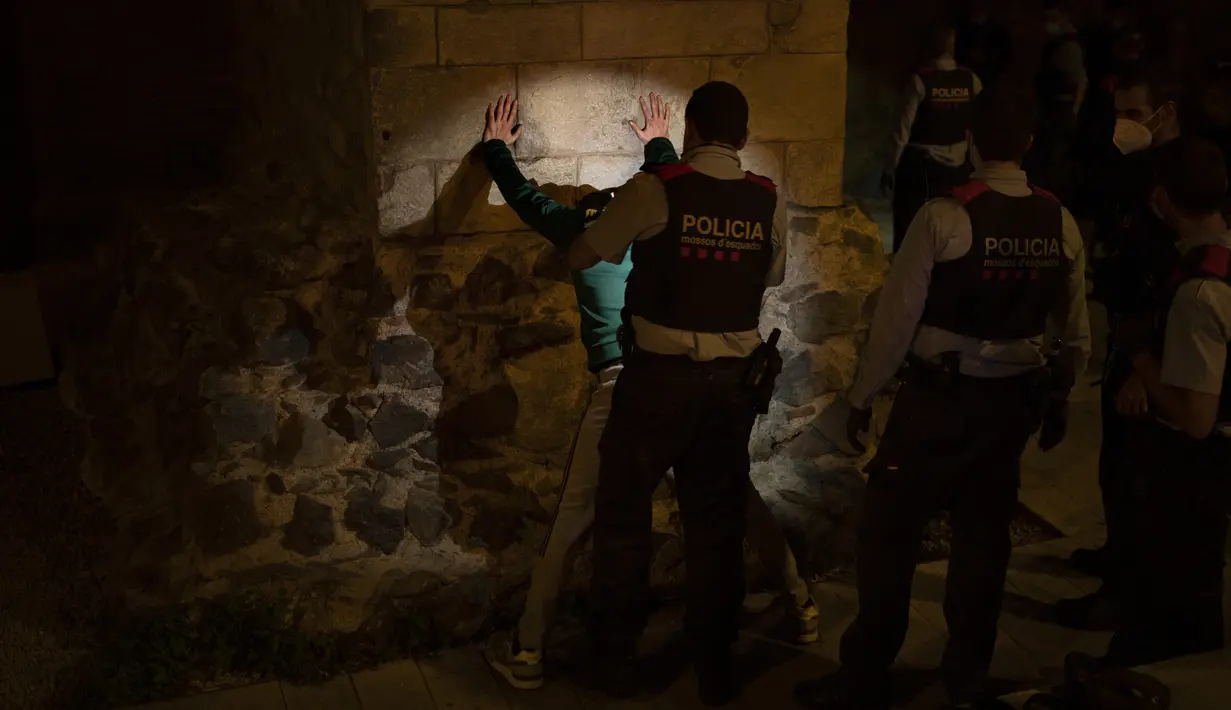 Seorang pria ditahan oleh Mossos d'Escuadra, kepolisian regional Catalonia, setelah jam malam di Barcelona pada 1 November 2020. Pemerintah Spanyol menetapkan pembatasan gerak atau jam malam yang berlaku pukul 22.00 untuk mengendalikan lonjakan kasus Covid-19. (AP Photo/Emilio Morenatti)
