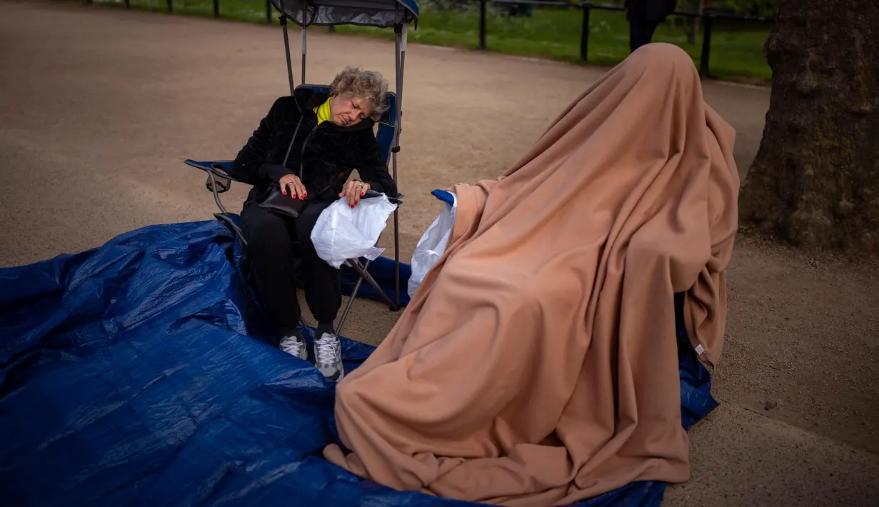 Dua penggemar kerajaan duduk di sepanjang rute Penobatan Raja di The Mall di London, Selasa, 2 Mei 2023. (AP Photo/Emilio Morenatti)
