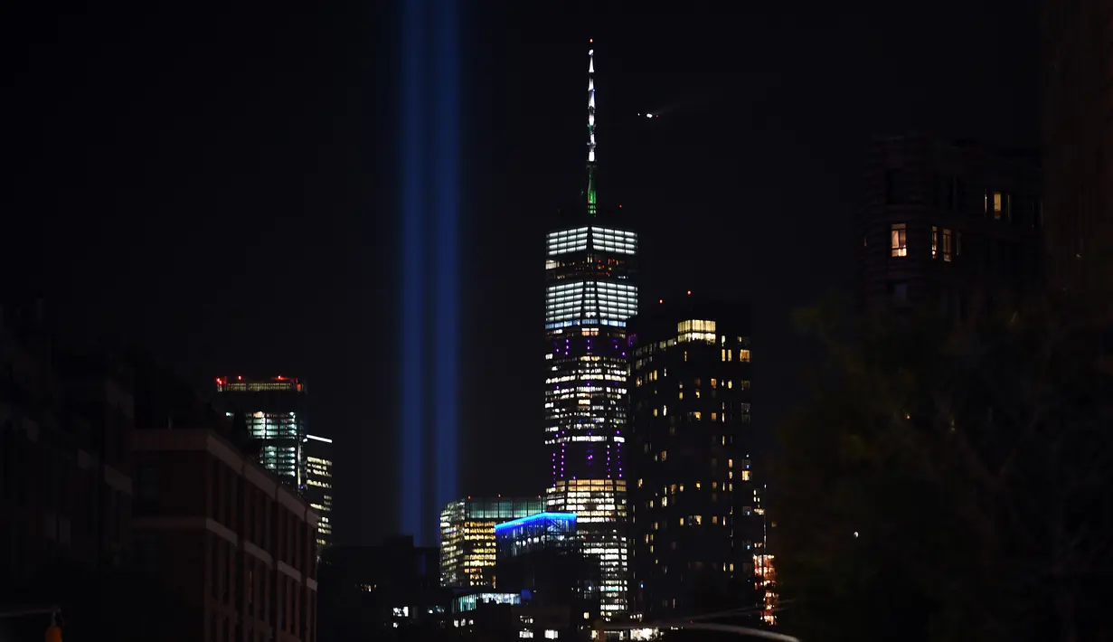 'Tribute in Light' dinyalakan untuk memperingati serangan gedung kembar WTC yang terlihat di dekat gedung One World Trade Center, New York City, Selasa (10/9/2019). Cahaya kembar itu jadi simbol menara kembar WTC yang hancur diserang kelompok pembajak pesawat 18 tahun silam. (Johannes EISELE/AFP)
