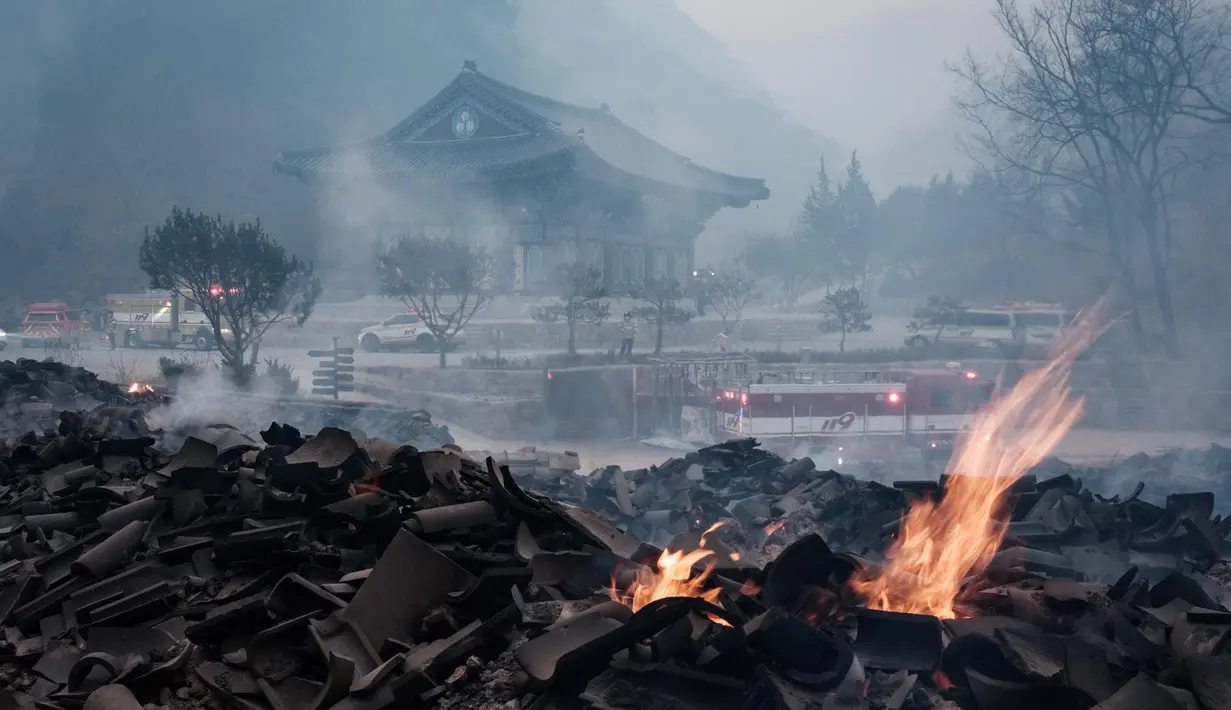 Bara api masih terlihat di antara puing-puing setelah sebagian besar bangunan hangus terbakar dalam kebakaran hutan di Kuil Gounsa, Uiseong, Korea Selatan pada 26 Maret 2025. (YASUYOSHI CHIBA/AFP)