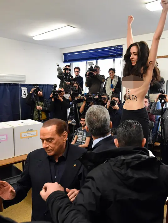 Mantan PM Italia dan pemimpin partai Forza Italia Silvio Berlusconi meninggalkan seorang wanita yang melakukan aksi topless saat pemungutan suara di Milan, Italia, Minggu (4/3). Aksi itu dilakukan di sebuah TPS. (Daniel Dal Zennaro/ANSA via AP)
