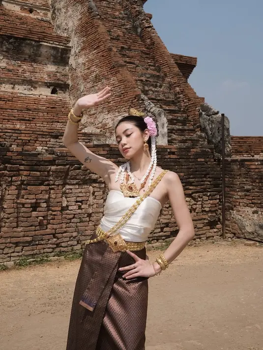 Regina juga berpose dengan gaya tarian khas Thailand, berlatar belakang reruntuhan kuil kuno yang memberikan nuansa budaya yang kental. Dengan sinar matahari yang terang, suasana menjadi semakin autentik, menciptakan keindahan warisan Thailand yang tak tertandingi. Penampilan Regina dalam balutan Chut Thai semakin menguatkan kesan bahwa ia adalah sosok yang menghargai budaya. (Liputan6.com/IG/@reginaaphx)