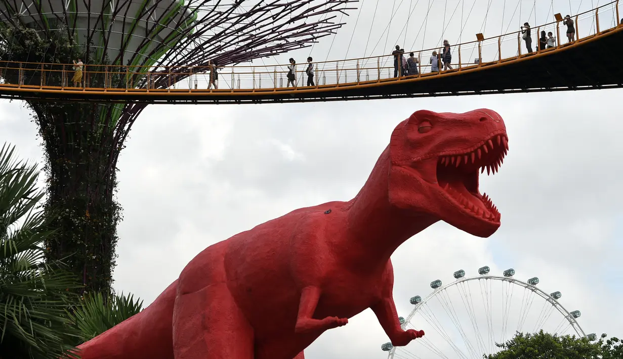 Pengunjung melihat patung dinosaurus di atas jembatan di Gardens by the Bay, Singapura, Senin (28/2). Rencananya akan dipamerkan sebanyak 11 dinosaurus beraneka warna untuk merayakan Festival Anak di Singapura. (AFP PHOTO / Roslan RAHMAN)