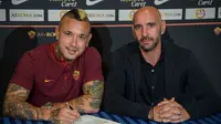 Di meja dengan taplak warna kebesaran Inter Milan, Radja Nainggolan (kiri) menandatangani kontrak baru hingga 2021 bersama AS Roma. (Twitter AS Roma)