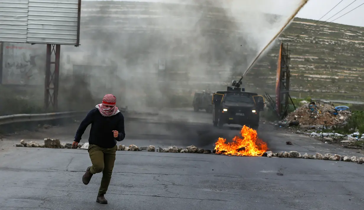 Wanita Palestina berlari menjauhi semprotan kendaraan meriam air Israel selama bentrokan dalam demonstrasi memperingati Hari Tanah di Tepi Barat, Sabtu (30/3). (Photo by ABBAS MOMANI/AFP)
