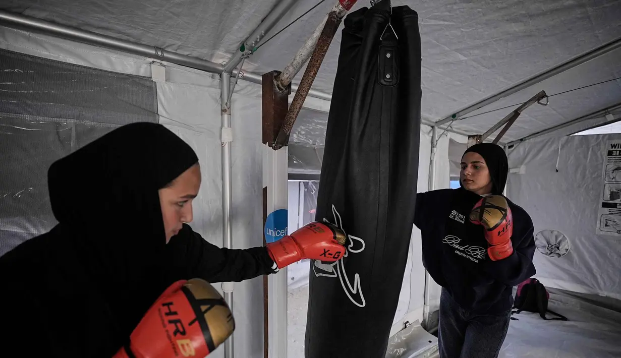 Selanjutnya, mereka memukul samsak seadanya yang digantung pada tiang penyangga tenda, seringkali tanpa sarung tangan tinju. Tampak dalam foto, gadis-gadis Palestina berlatih di klub tinju sementara di dalam tenda di Kota Gaza, Selasa, 5 Mei 2026. (AP Photo/Jehad Alshrafi)