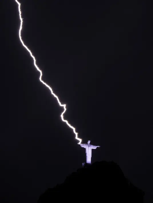 Petir menyambar tangan Christ the Redeemer atau Patung Kristus Penebus di gunung Corcovado di Rio de Janeiro, Brasil, Selasa (21/2/2023). Laman History Hit mencatat kalau patung tersebut pernah disambar petir hingga terbakar dan rusak pada 2008 dan 2014. (Photo by MAURO PIMENTEL / AFP)
