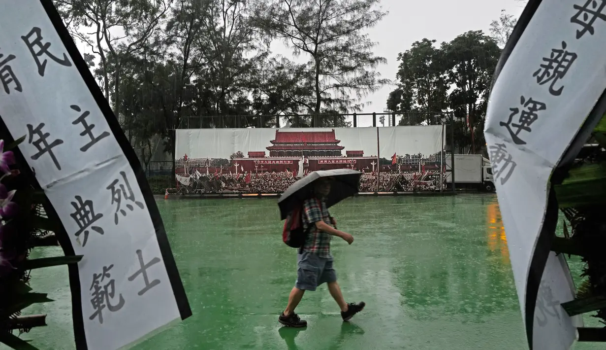 Seorang pria berjalan melewati spanduk yang menampilkan Lapangan Tiananmen, Beijing, yang dipajang di Taman Victoria Hong Kong (4/6/2019). Puluhan ribu orang diperkirakan akan menghadiri acara nyala lilin tahunan untuk para korban tragedi Tiananmen 1989. (AP Photo/Vincent Yu)