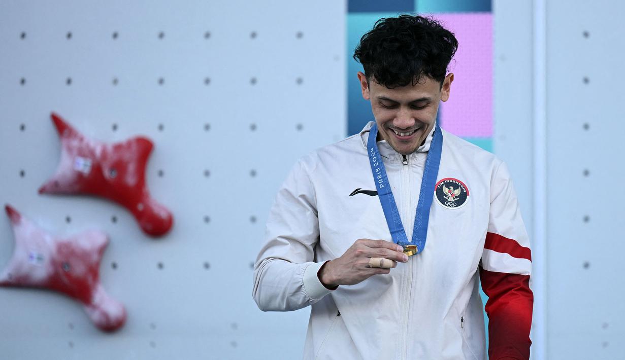 Atlet panjat tebing Indonesia, Veddriq Leonardo memandangi medali emasnya saat di atas podium cabang olahraga panjat tebing nomor speed Olimpiade Paris 2024 di Le Bourget Sport Climbing Venue, Paris, Prancis, Kamis (08/08/2024). (AFP/Jonathan Nackstrand)
