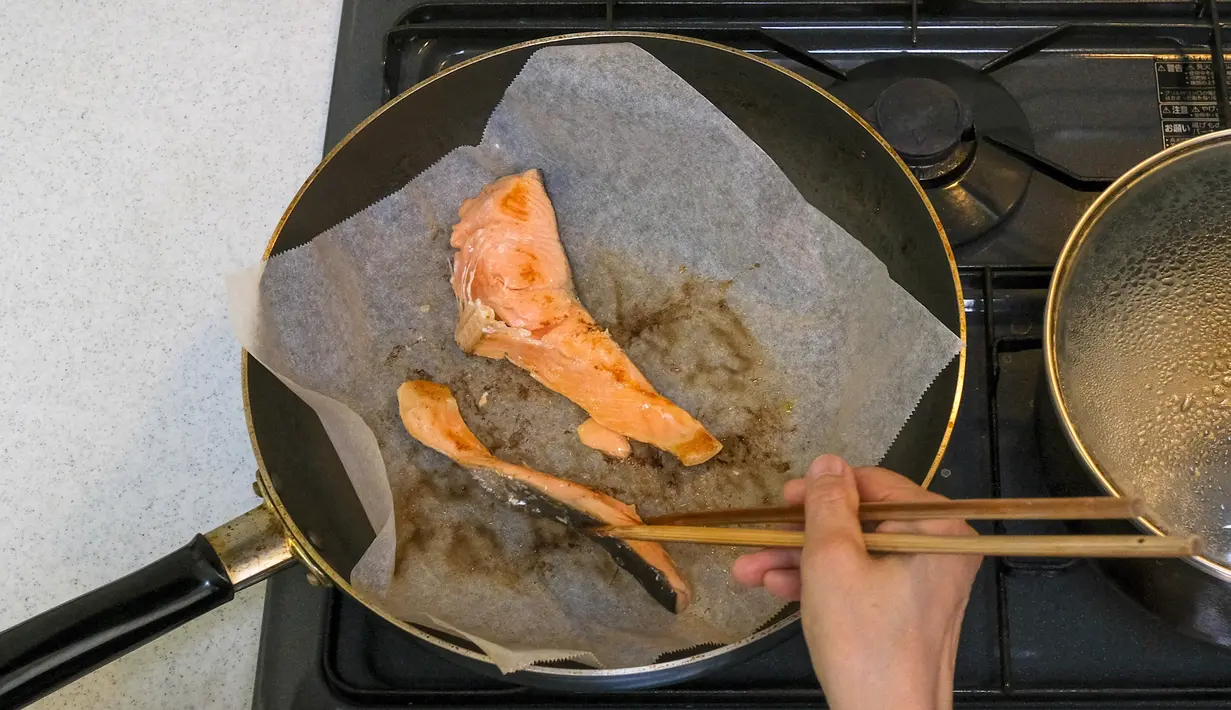 Pemenang kontes resep makanan Desa Olimpiade Tokyo 2020 Yoko Nishimura memasak sepotong salmon di Tokyo, Jepang, 12 Juli 2021. Desa Olimpiade Tokyo 2020 jadi kesempatan atlet untuk mencicipi masakan Jepang yang terkenal. (KAZUHIRO NOGI/AFP)