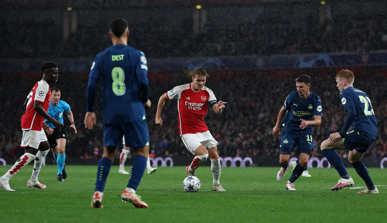 Pemain Arsenal, Martin Odegaard (tengah) berusaha melewati adangan dari sejumlah pemain PSV Eindhoven pada laga Grup B Liga Champions 2023/2024 di Emirates Stadium, London, Kamis (21/09/2023) dini hari WIB. (AFP/Adrian Dennis)