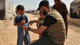 Seorang sukarelawan membagikan pakaian kepada anak-anak Suriah di sebuah kamp di pinggiran kota Dana yang dikuasai pemberontak, di sebelah timur perbatasan Turki-Suriah di provinsi barat laut Idlib (30/4/2022). Umat Islam seluruh dunia bersiap untuk merayakan Idul Fitri yang menandai akhir bulan puasa Ramadhan. (AFP/Aaref Watad)