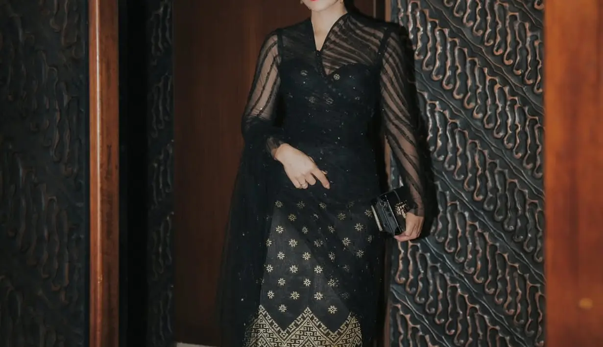 Wulan Guritno memilih busana bernuansa gelap yang memancarkan aura anggun dan elegan. Ia mengenakan kebaya hitam transparan dengan motif tradisional yang dipercantik bordir emas, sebuah karya dari Tangan Prive.