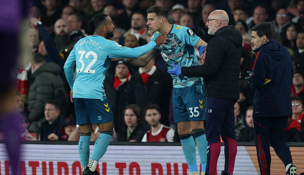 Gelandang Southampton, Theo Walcott (kiri) berusaha membujuk Jan Bednarek untuk mengikuti anjuran tim medis agar tak melanjutkan pertandingan saat menghadapi Arsenal pada laga Liga Inggris 2022/2023 di Emirates Stadium, London (21/4/2023). (AFP/Adrian Dennis)