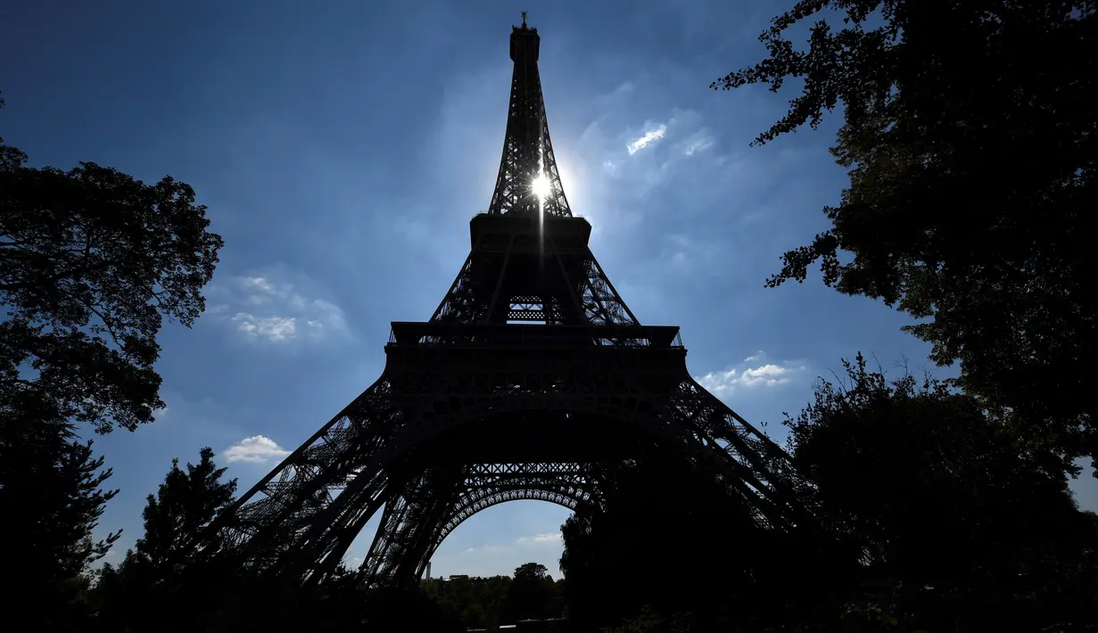 Matahari bersinar di antara struktur Menara Eiffel, Paris, Kamis (2/8). Perubahan tiket membuat  antrean turis begitu panjang, staf pun protes dan mogok kerja sehingga Eiffel terpaksa ditutup. (AFP PHOTO/GERARD JULIEN)