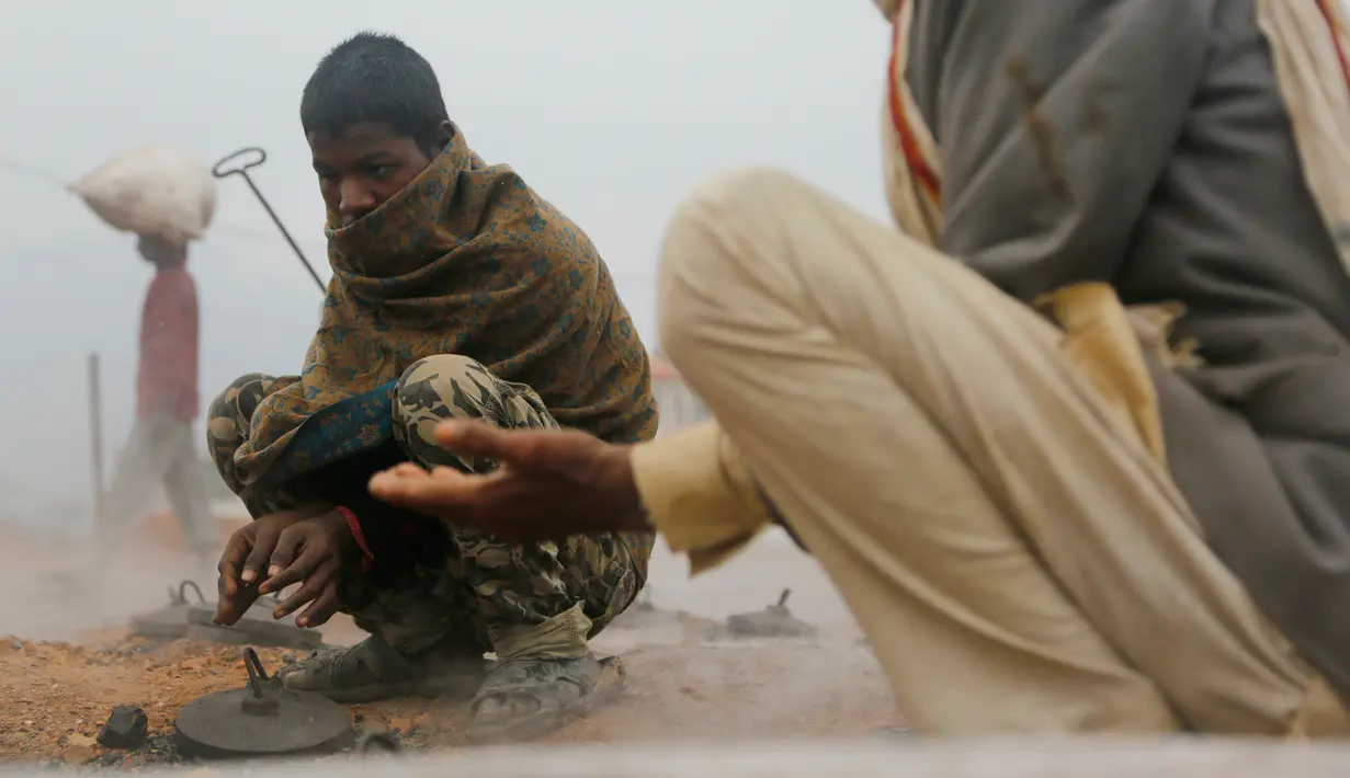 Pekerja migran India menghangatkan dirinya di atas tungku di sebuah pabrik batu bata di pinggiran Kathmandu. Ribuan pekerja migran India datang ke Nepal untuk bekerja di pabrik batu bata. (AP Photo/Niranjan Shrestha)