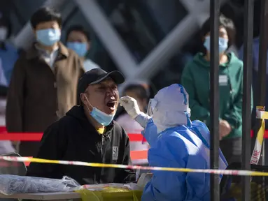 Seorang pekerja yang mengenakan alat pelindung diri menyeka tenggorokan seorang pria saat tes COVID-19 di tempat pengujian setelah pihak berwenang memerintahkan putaran ketiga dari tiga tes COVID-19 berturut-turut untuk penduduk di Distrik Chaoyang, Beijing, China, Sabtu (7/5/2022). (AP Photo/Mark Schiefelbein)