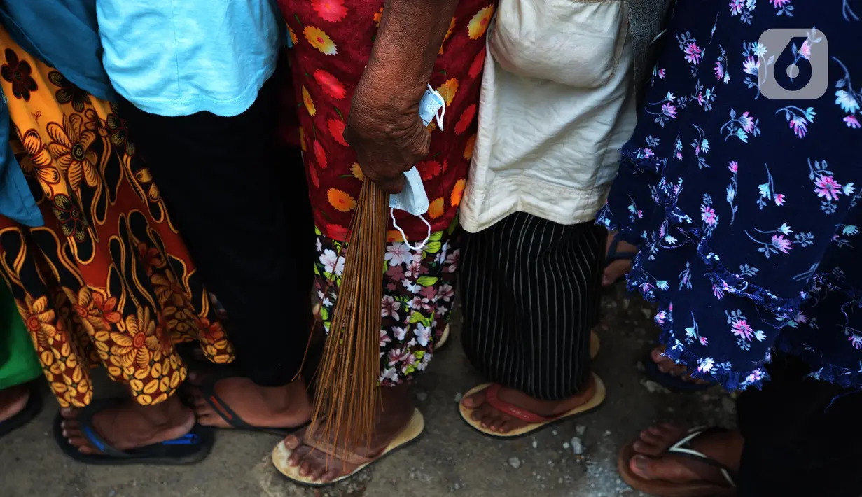 Warga membawa sapu lidi saat antre pembagian sembako di TPU Malaka, Pondok Kopi, Jakarta, Jumat (4/3/2022). Pembagian sejumlah sembako secara gratis yang diperuntukan bagi kaum duafa ini berupa beras dan minyak goreng. (merdeka.com/Imam Buhori)
