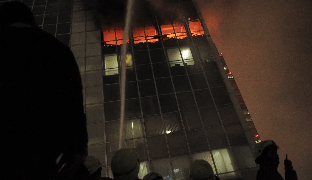 Lokasi yang tinggi dan hembusan angin menyulitkan petugas menjinakkan si jago merah. Terlihat petugas menyemprotkan api dari gedung sebelahnya, Jakarta, Senin (9/3/2015).(Liputan6.com/Faizal Fanani)