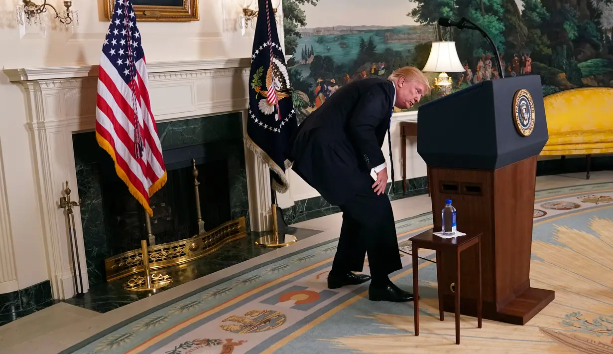 Presiden AS, Donald Trump mencari botol air minum disela pidatonya di Ruang Diplomatik, Gedung Putih, Rabu (15/11). Trump sempat berhenti di tengah pemaparannya untuk mencari botol air minum namun tidak bisa menemukannya. (AP/Pablo Martinez Monsivais)