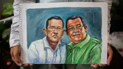 Pelukis Nikaragua Fernando Torres, 28, memegang lukisan saudara laki-laki Adan Augusto Alonso (kiri) dan Maximo Guillerno Alonso (kanan), dokter medis yang meninggal akibat COVID-19 yang terjangkit saat memberikan bantuan kepada orang lain di Managua pada 21 Juni 2020. (INTI OCON/AFP)
